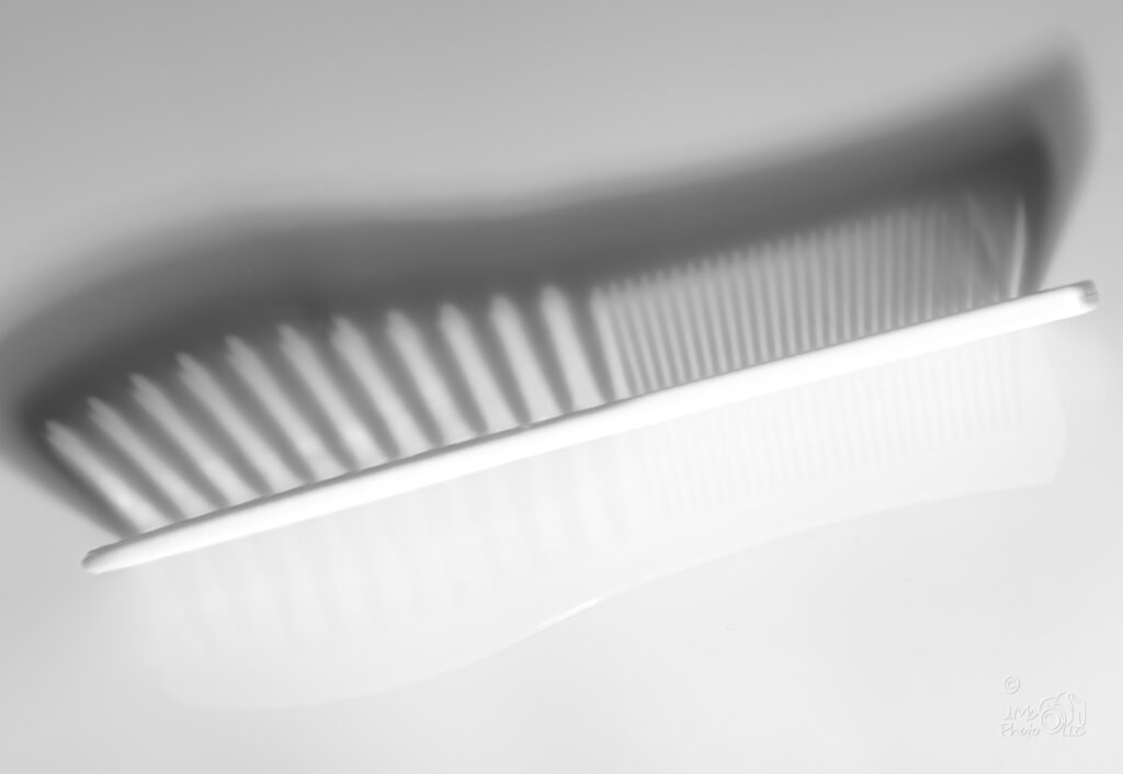 High key black and white photo of a comb showing shadow and reflection