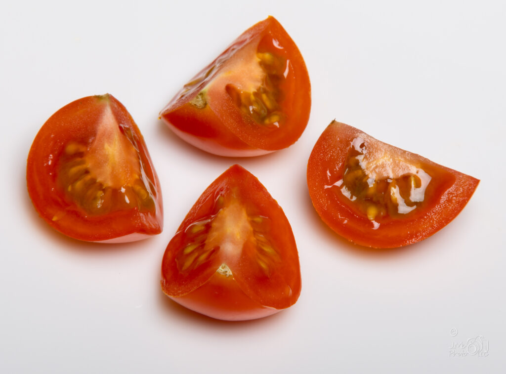 Small tomato sliced into quarters on white background