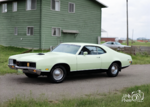 Restored photograph of a classic car parked outside a green house